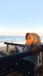 Boy sitting on beach by sea against sky