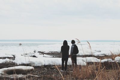 Rear view of friends standing at frozen beach against sky