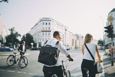 Rear view of male and female colleagues standing with bicycle on road in city