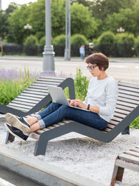 Woman sits with laptop on urban park bench. freelancer at work. student learns remotely. 