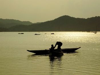 Silhouette people on boat sailing in sea against clear sky