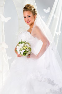 Portrait of smiling bride holding bouquet while standing by arch