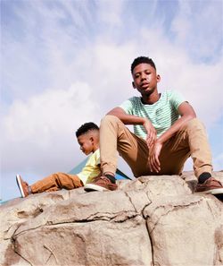 Siblings sitting on rock against sky