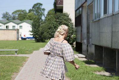 Rear view of woman walking on footpath by building