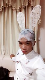 Portrait of man wearing costume rabbit ears against curtain