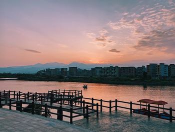 Scenic view of river by buildings against sky during sunset