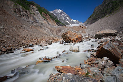 Scenic view of stream flowing through rocks against sky