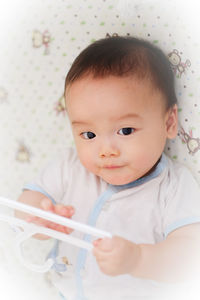 High angle portrait of baby boy playing with coathanger while lying on bed at home