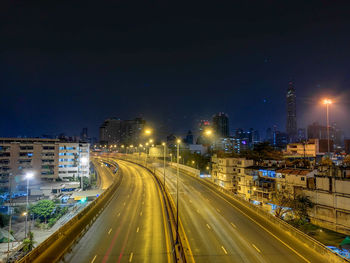 High angle view of light trails on road amidst buildings in city at night