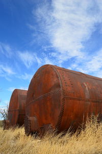 Rusty metal tanks on field against sky