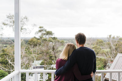 Rear view of couple with arms around waist standing in balcony