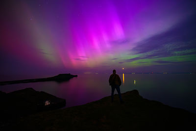 Rear view of man standing on cliff top against northern lights aurora boralis 