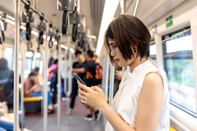 Side view of woman using smart phone while standing in train