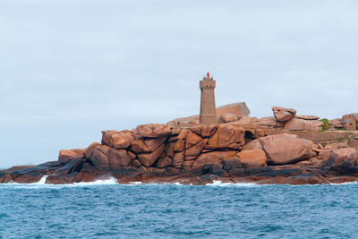 Lighthouse on rocks by sea against sky