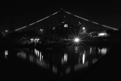 Illuminated city by river against sky at night