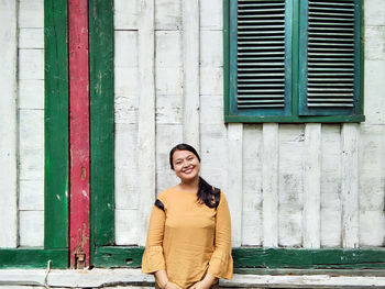 Portrait of smiling young woman standing against window