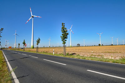 Windmills by empty road against clear blue sky