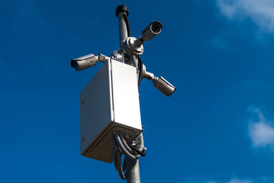 Low angle view of security cameras against blue sky during sunny day