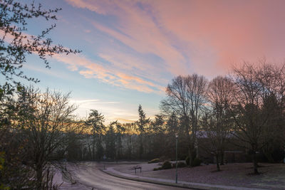 Road amidst bare trees against sky during sunset