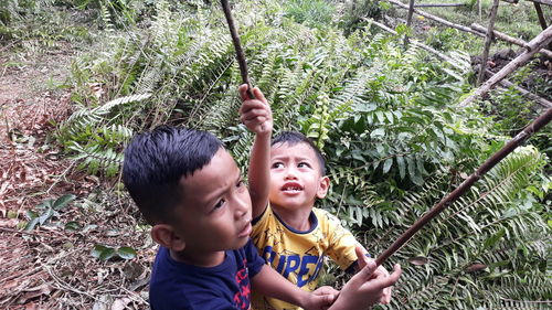 Smiling brothers holding sticks while standing outdoors