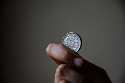 Close-up of hand holding coin against black background