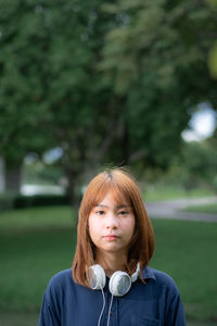 Portrait of young woman with headphones standing in park