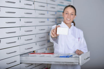 Portrait of female pharmacist holding box in medicine storage compartment