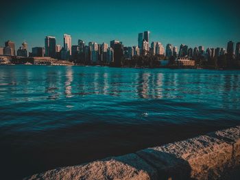 Sea by modern buildings against clear blue sky