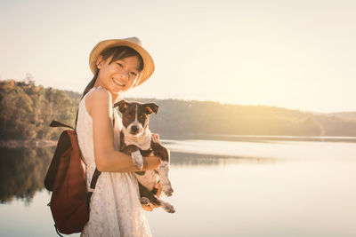 Portrait of girl with dog standing against lake during sunset