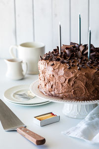 A large chocolate frosted cake with candles ready for lighting.