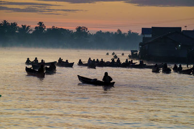 Silhouette people on boat in sea against sky during sunset