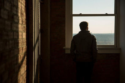 Rear view of man looking through window in building