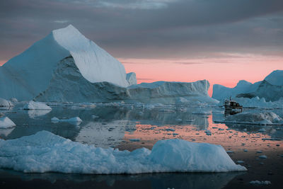 Iceberg in sea against cloudy sky during sunset