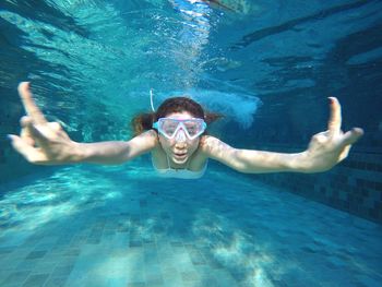 Portrait of woman swimming in pool showing peace sign