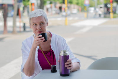 An aged woman with bob cut drink water from plastic bottle at the cafe table