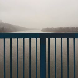 Close-up of railing by lake against sky