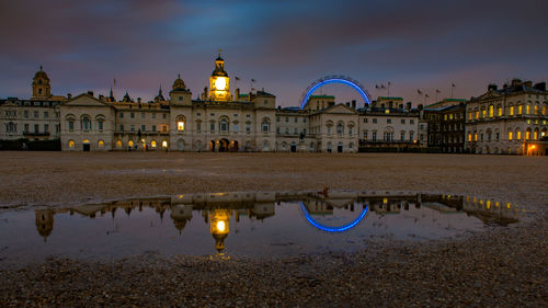 Illuminated london eye by palace of whitehall against sky at night