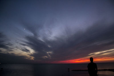 Silhouette people looking at sea against sky during sunset