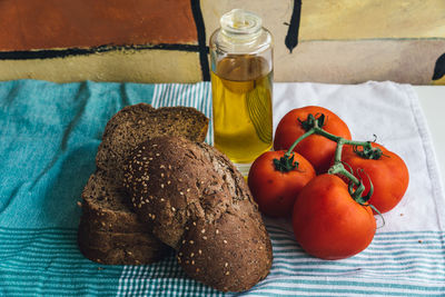 High angle view of brown bread with olive oil bottle and tomatoes on tablecloth at table