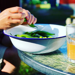 Close-up of male hands over a bowl peeling fava beans outdoors on a sunny summer day 