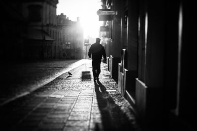 Silhouette man walking on sidewalk in city