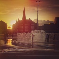 People at fountain in city against sky during sunset