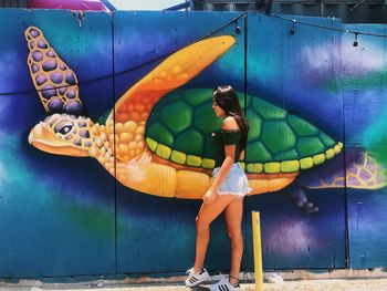 Woman with umbrella standing against graffiti wall