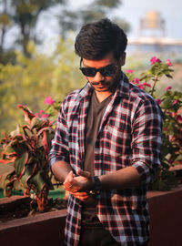 Young man wearing sunglasses standing against plants