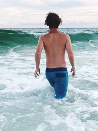 Rear view of shirtless man wading in sea