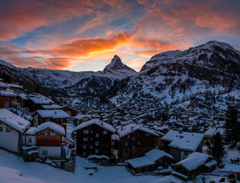Snow covered houses and buildings against sky during sunset
