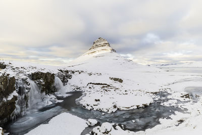 Scenic view of waterfall and snowcapped mountain against sky