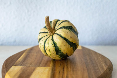 A single mini green and white decorative pumpkin displayed on a wooden chopping board