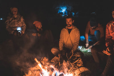 People sitting by bonfire at night