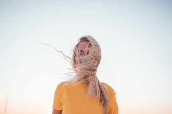 Woman with tousled hair standing against sky